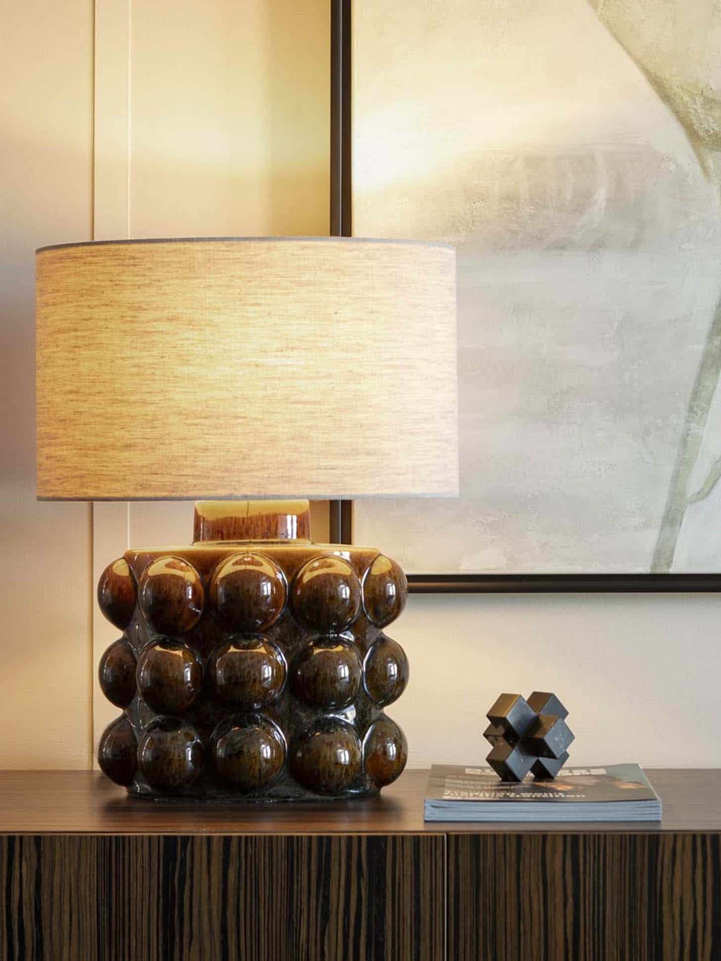 Table lamp styling detail with sculptural ceramic base and warm linen shade on console table in executive office